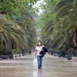 Una mujer ataviada con una mascarilla camina por el Paseo del Parque de Málaga