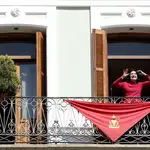 Una mujer saluda después de colocar un gran pañuelo con la imagen de San Fermín en el balcón