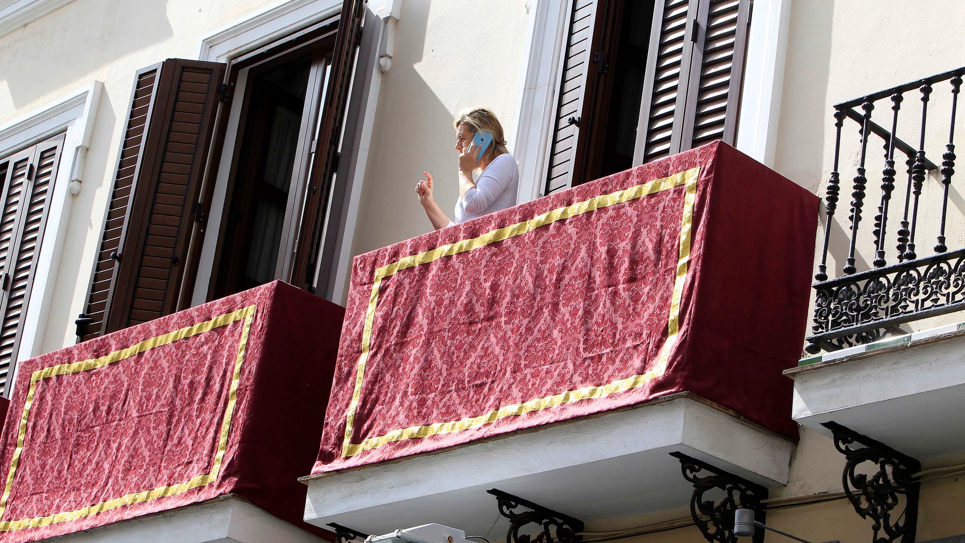 Una mujer habla desde su balcón en Sevilla, engalanado para la Semana Santa