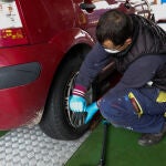 Un trabajador de un taller protegido con una mascarilla arregla la rueda de un coche