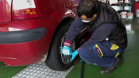 Un trabajador de un taller protegido con una mascarilla arregla la rueda de un coche