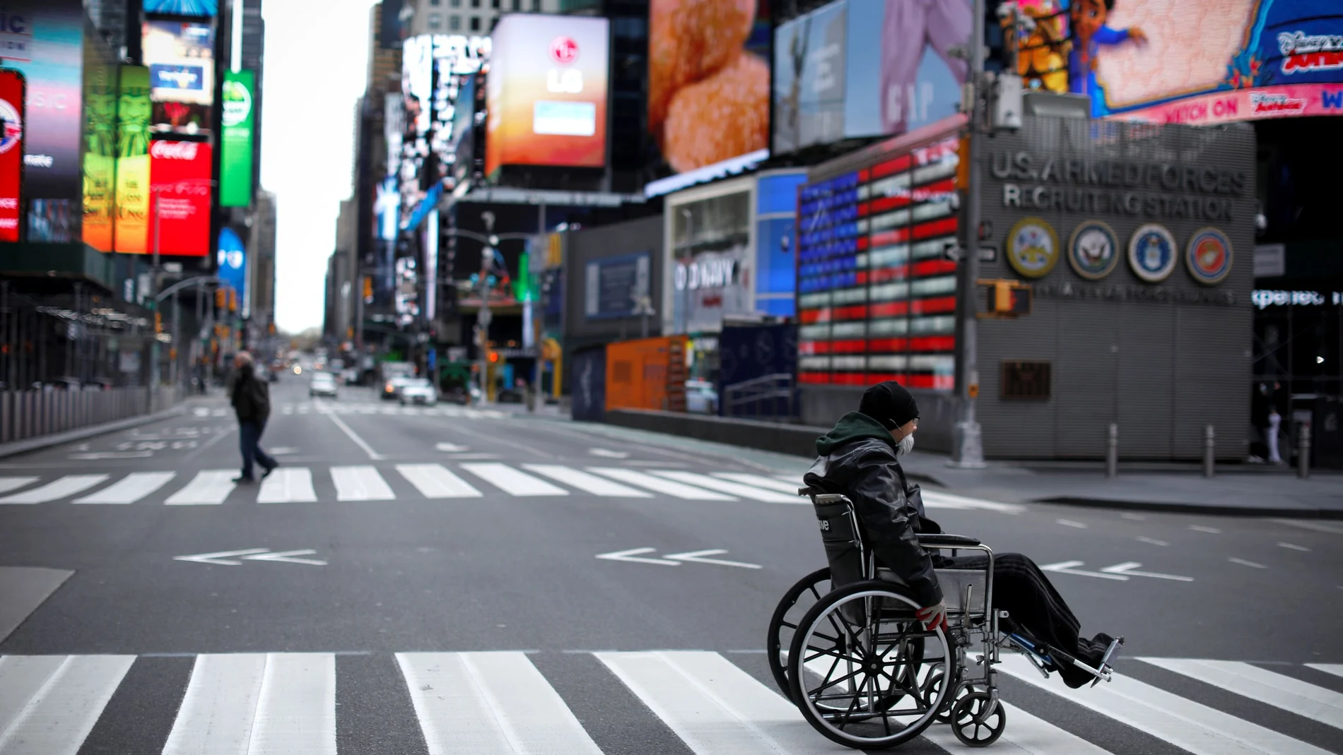 Un hombre en silla de ruedas y con mascarilla cruza una calle en Nueva York