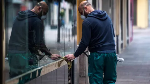 Un trabajador de la limpieza limpia los cristales de una tienda en el centro de Córdoba