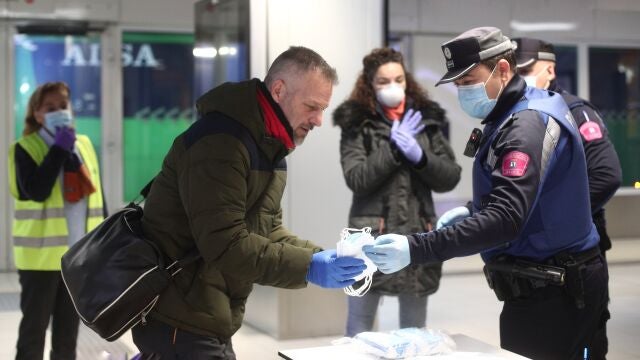 Un agente de la Policía Municipal de Madrid reparte mascarillas a pasajeros en una mesa en el acceso al intercambiador de autobuses de Avenida de América el día en el que se reactiva la actividad laboral no esencial en las empresas cuyos empleados no puedan teletrabajar cuando se cumple un mes desde el inicio del estado de alarma decretado a consecuencia del coronavirus, en Madrid (España), a 13 de abril de 2020.13/04/2020;COVID-19;CORONAVIRUS;ESTADO DE ALARMA;DESCONFINAMIENTO PARCIAL;CRISIS;PANDEMIAEduardo Parra / Europa Press13/04/2020