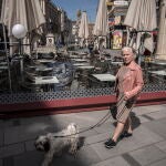 Un hombre sentado en una terraza -con la mascarilla bajada- mientras una anciana -sin mascarilla- pasea su mascota este mes de abril en plena pandemia