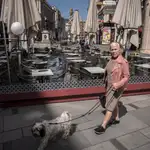 Un hombre sentado en una terraza -con la mascarilla bajada- mientras una anciana -sin mascarilla- pasea su mascota este mes de abril en plena pandemia