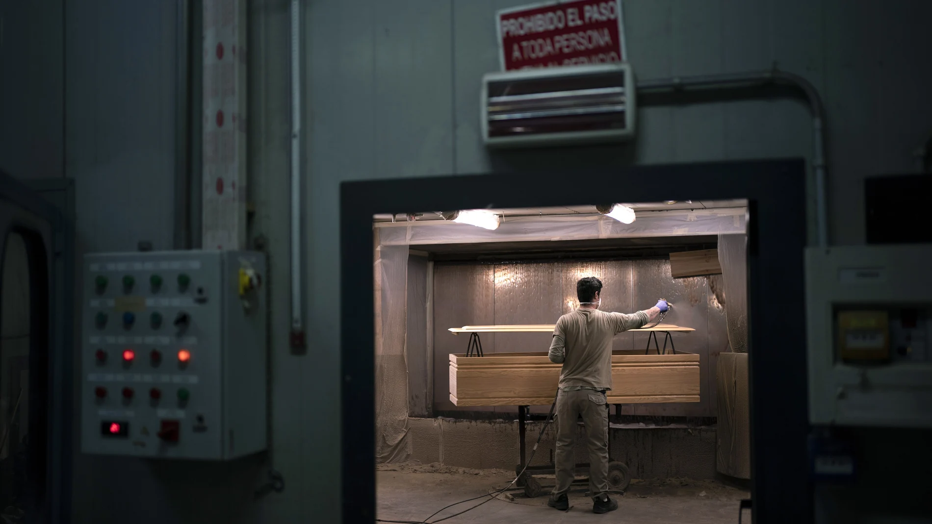 Un trabajador aplica barniz a un ataúd en la fabrica de Eurocoffin en Barcelona que ha triplicado su producción desde que comenzó la pandemia