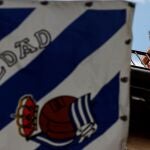 Un aficionado del Athletic silba junto a una bandera de la Real Sociedad
