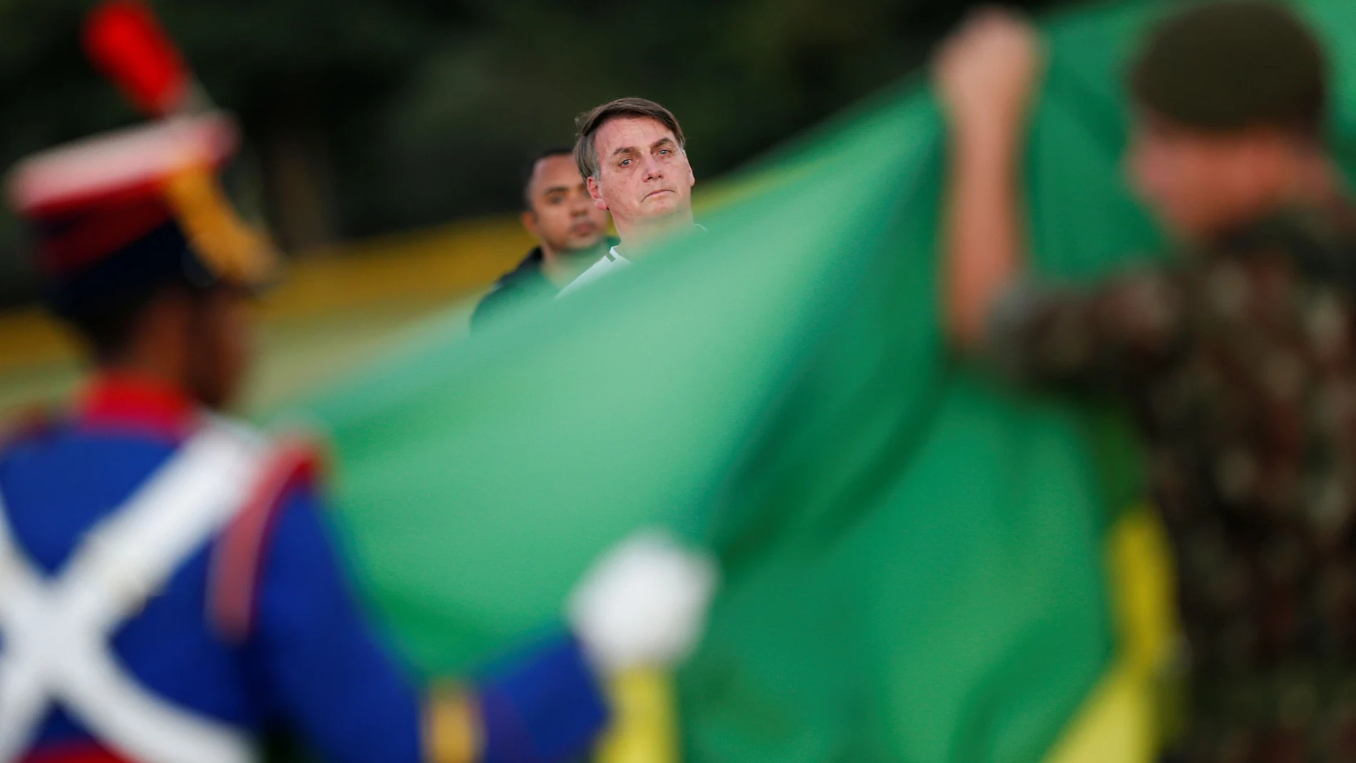 Brazil's President Jair Bolsonaro observes ceremony to remove the Brazilian National flag, as he walks outside the Alvorada Palace, amid the coronavirus disease (COVID-19) outbreak in Brasilia