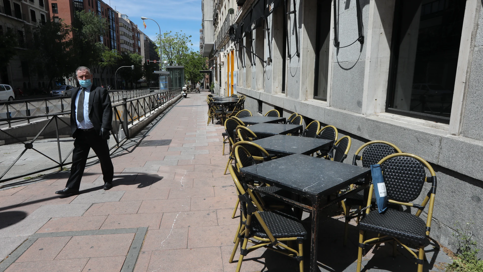 Un hombre con mascarilla pasa junto a una terraza cerrada de un bar en el centro de Madrid