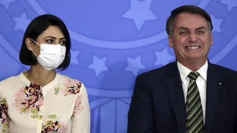 Brazil's President Jair Bolsonaro smiles sitting next to his wife Michelle Bolsonaro wearing a protective face mask, during the swearing ceremony of his new justice minister, at the Planalto presidential palace, in Brasilia, Brazil, Wednesday, April 29, 2020. (AP Photo/Eraldo Peres)