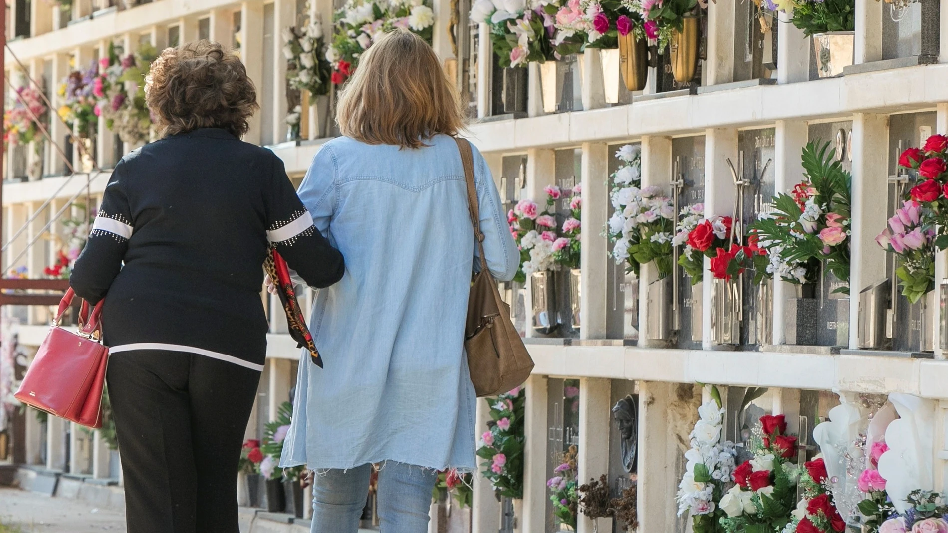 Dos mujeres caminan por el cementerio tras colocar flores en la tumba de sus familiares en Zaragoza.