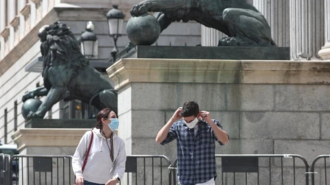 Una pareja con mascarillas pasa por delante de la fachada del Congreso de los Diputados