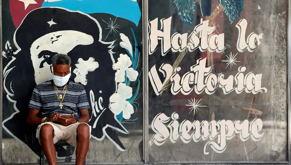 HAB01. LA HABANA (CUBA), 07/05/2020.- Un hombre con tapabocas revisa en su celular, junto a un graffitis con la imagen del guerrillero argentino-cubano Ernesto Che Guevara, este jueves en La Habana (Cuba). efe/Ernesto Mastrascusa