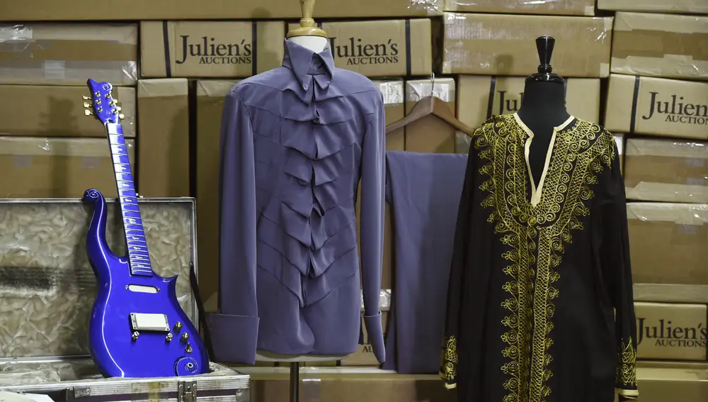 A blue &quot;cloud&quot; guitar made in the 1980s for the late musician Prince is displayed alongside some of his clothing, at Julien's Auctions warehouse, Wednesday, May 6, 2020, in Culver City, Calif. In the middle is a purple stage outfit from Prince's New Power Soul Tour in the late 1990s and at right is a black tunic that was made for him by his former wife Mayte and worn at home. Julien's Auctions announced Monday that the items will be part of a major music artifacts auction taking place on June 19 and 20 in Beverly Hills and online. (AP Photo/Chris Pizzello)