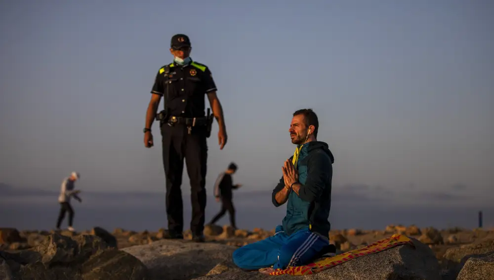 Un agente de policía se dirige a una persona que practica yoga en el espigón. (AP Photo/Emilio Morenatti)