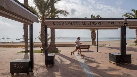 Dos personas pasan junto a la terraza de un restaurante en el paseo de la playa de Barnuevo, San Javier