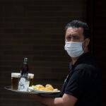 Un camarero protegido con mascarilla sirve en los veladores de un bar
