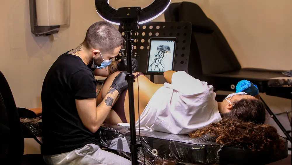 Un tatuador, en su estudio, realiza un tatuaje a una mujer