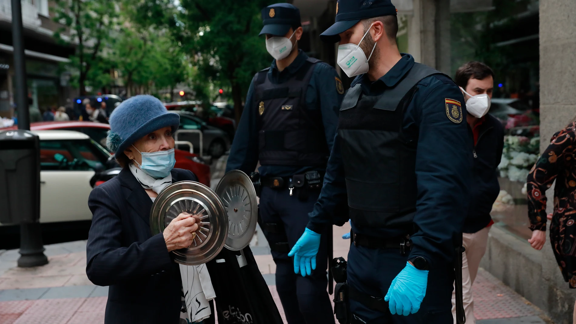Una mujer del distrito de Salamanca manifestándose con dos cacerolas, pasa al lado de dos agentes