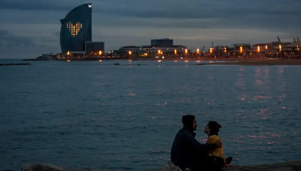 14 May 2020, Spain, Barcelona: A couple sits on the Barceloneta beach at sunset while behind them the W Hotel lights up a heart in its windows in gratitude for the work of the health workers. Photo: Jordi Boixareu/ZUMA Wire/dpa14/05/2020 ONLY FOR USE IN SPAIN