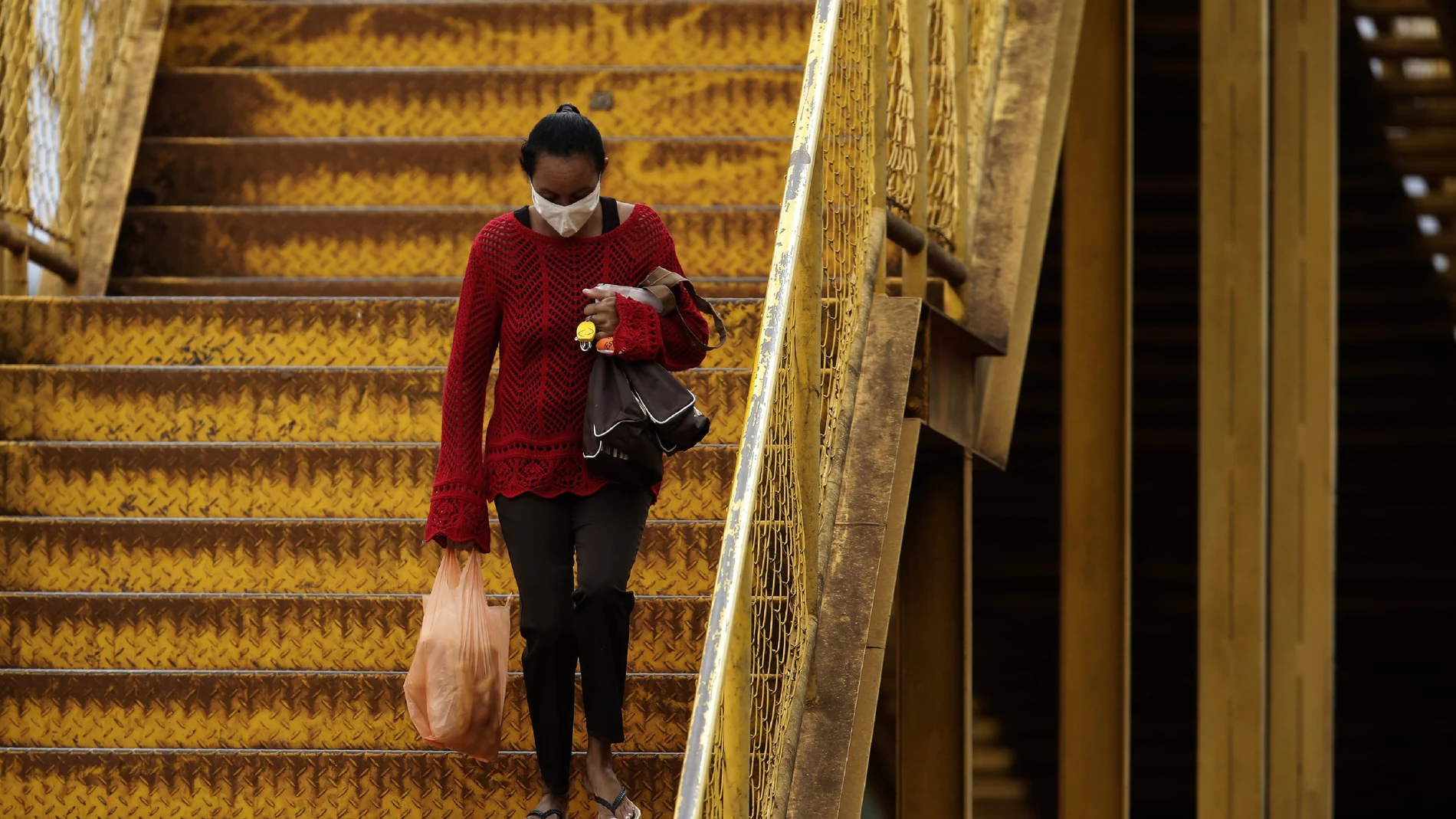 A woman wearing a mask against the spread of the new coronavirus walks down a set of stairs in Valparaiso, Brazil, Wednesday, May 20, 2020. Valparaiso, 40 km. from Brasilia, appears in the statistics as one of the cities in the state of Goias with a high incidence of COVID-19. (AP Photo/Eraldo Peres)
