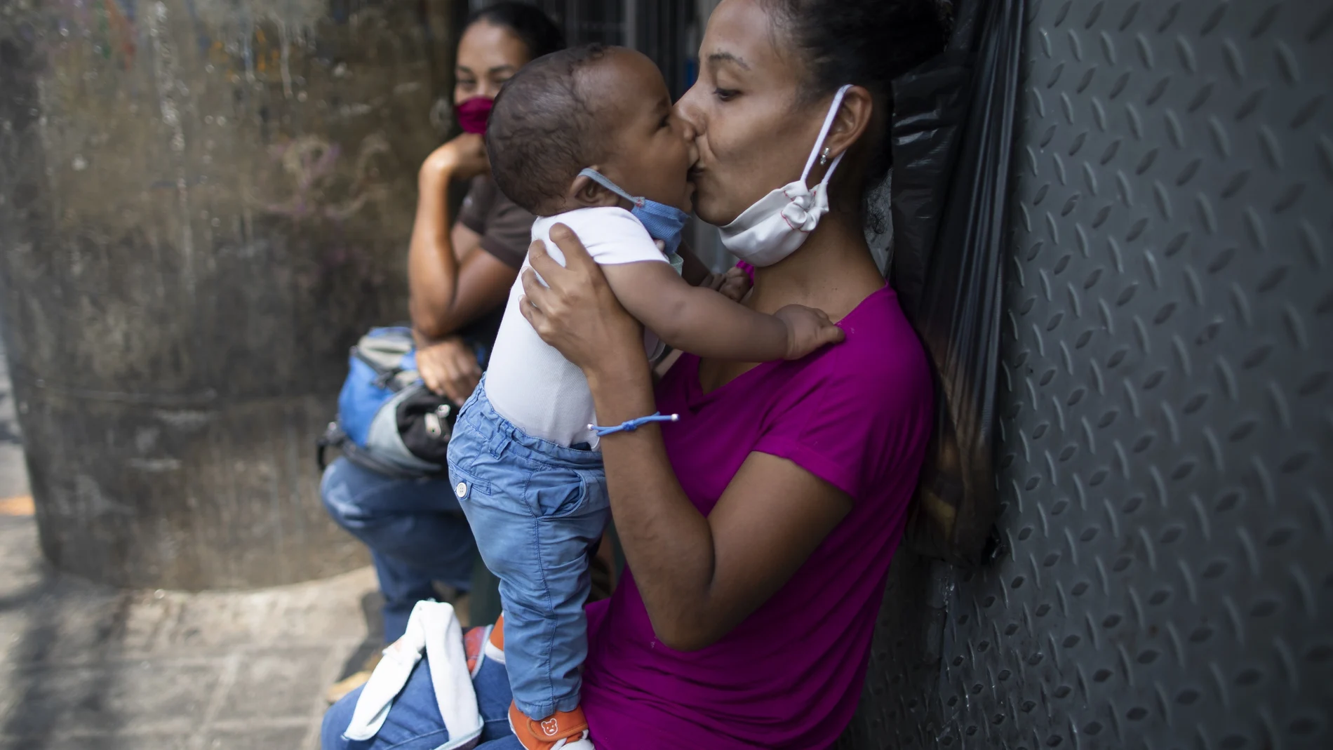 Una madre besa a su bebé, ambos con mascarillas, en una calle de Caracas, Venezuela
