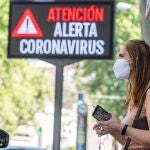 Una mujer espera el autobús junto a un panel informativo en Sevilla