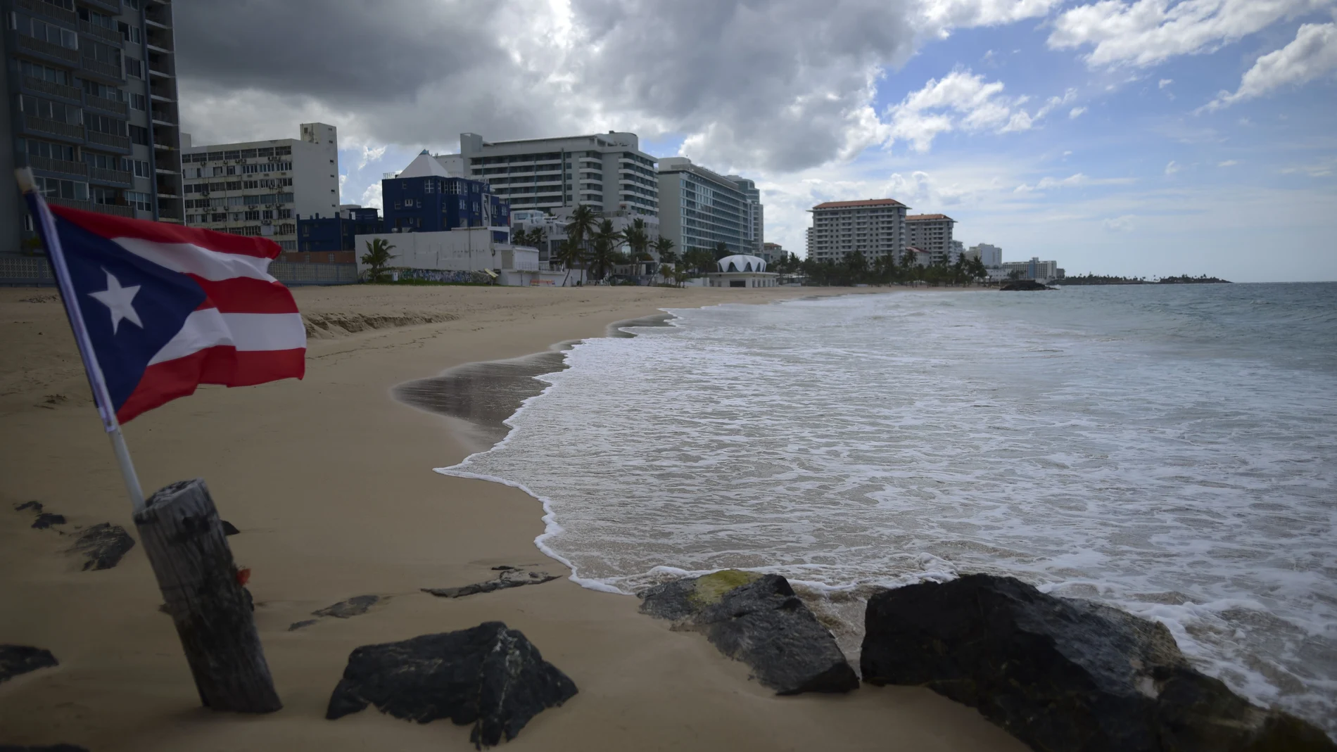 A Puerto Rican flag flies on an empty beach at Ocean Park, in San Juan, Puerto Rico, Thursday, May 21, 2020. Puerto Rico is cautiously reopening beaches, restaurants, churches, malls, and hair salons under strict conditions as the U.S. territory emerges from a two-month lockdown despite dozens of new coronavirus cases reported daily. (AP Photo/Carlos Giusti) PUERTO RICO OUT-NO PUBLICAR EN PUERTO RICO