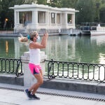 Una mujer con mascarilla hace deporte y toma fotos junto al Estanque por la calle Nicaragua en el Parque del Retiro de Madrid