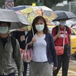 Taiwaneses caminan con mascarilla y paraguas por el centro de Taipéi