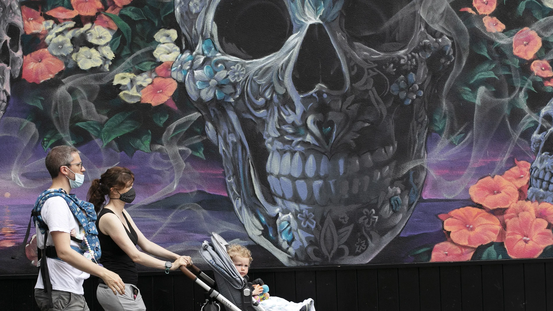 Unos padres con mascarillas pasean por Nueva York frente a un mural