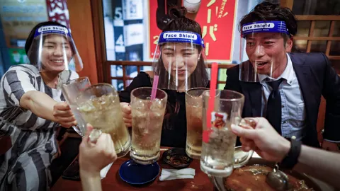Un grupo de amigos con protectores de plástico brindan en un pub de Osaka (Japón)