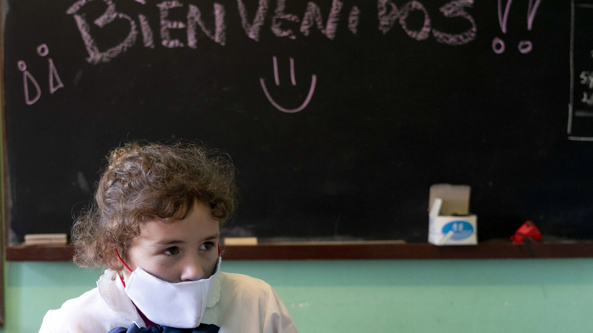 A girl wearing a face mask amid the new coronavirus pandemic attends class where the chalkboard reads in Spanish "Welcome!" at a rural school near Empalme Olmos, Uruguay, Monday, June 1, 2020. Some children returned to school Monday in some areas as Uruguay's total lockdown begins to ease. (AP Photo/Matilde Campodonico)
