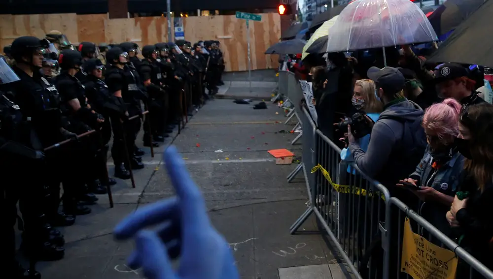 Un manifestante levanta una mano mientras la Policía de Seattle vigila una marcha en la que los manifestantes usan paraguas como escudo