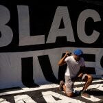 Un hombre se arrodilla en un enorme cartel que reza "las vidas negras importan" tras la masiva protesta de Washington este fin de semana