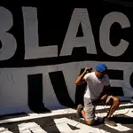 Un hombre se arrodilla en un enorme cartel que reza &quot;las vidas negras importan&quot; tras la masiva protesta de Washington este fin de semana