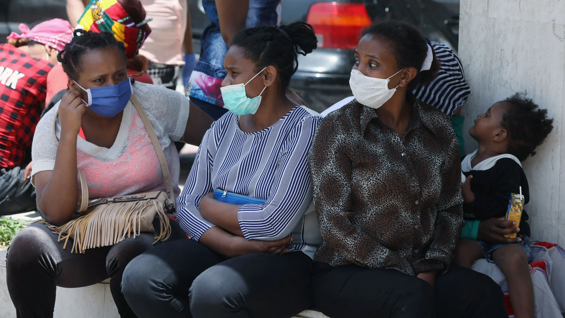 Ethiopian domestic workers wearing masks sit together with their belongings in front of the Ethiopian consulate in Hazmiyeh