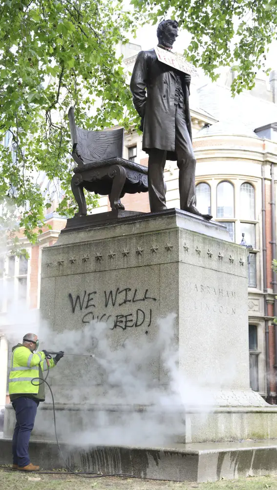 Un trabajador intenta limpiar un grafiti de la base de la estatua del presidente Lincoln en Londres. También ha sido protegida por vallas