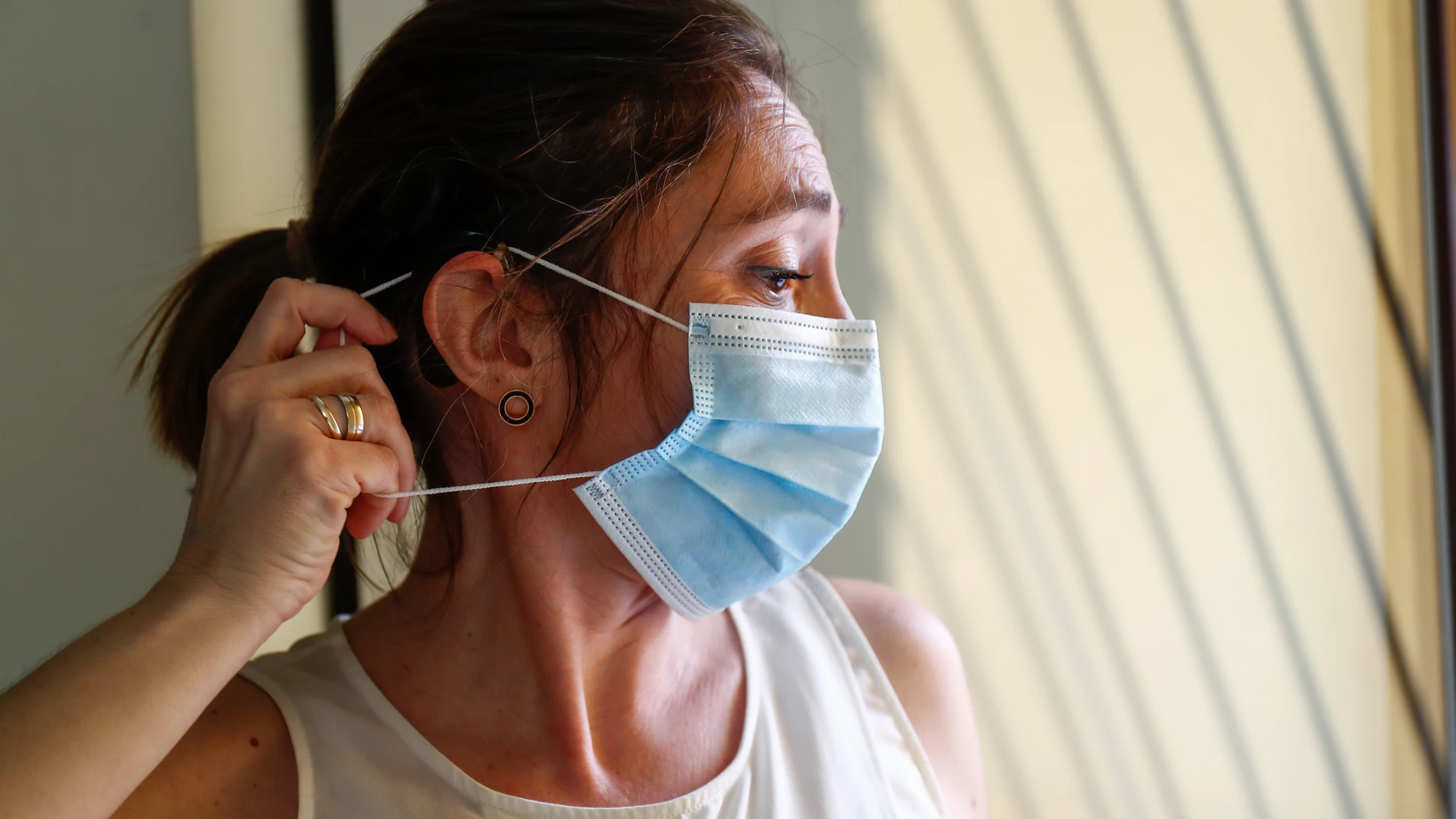 Loli, profesora, usuaria de un implante coclear y miembro de FIAPAS (Confederación Española de Familias de Personas Sordas), se coloca una mascarilla intentando que no se le enganche con el implante