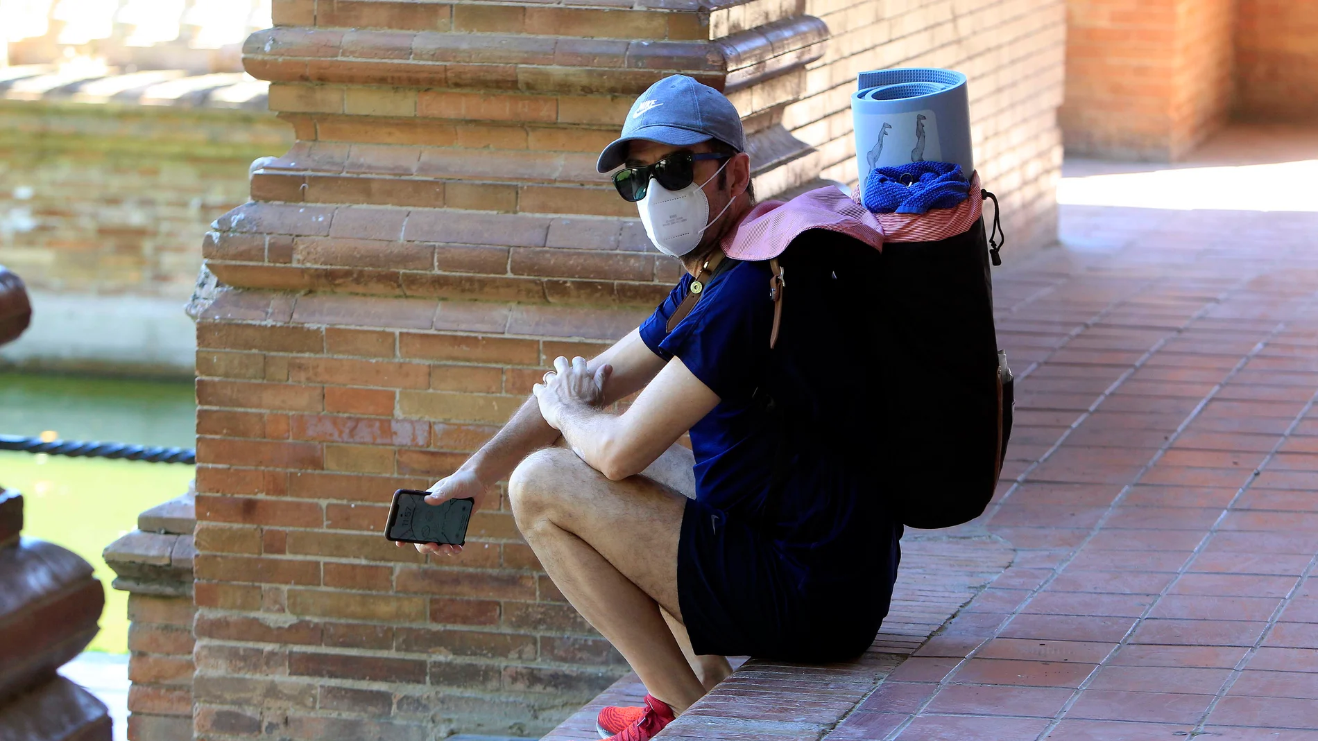 Una persona, equipada con mascarilla, descansa sobre los escalones de la Plaza de España de Sevilla