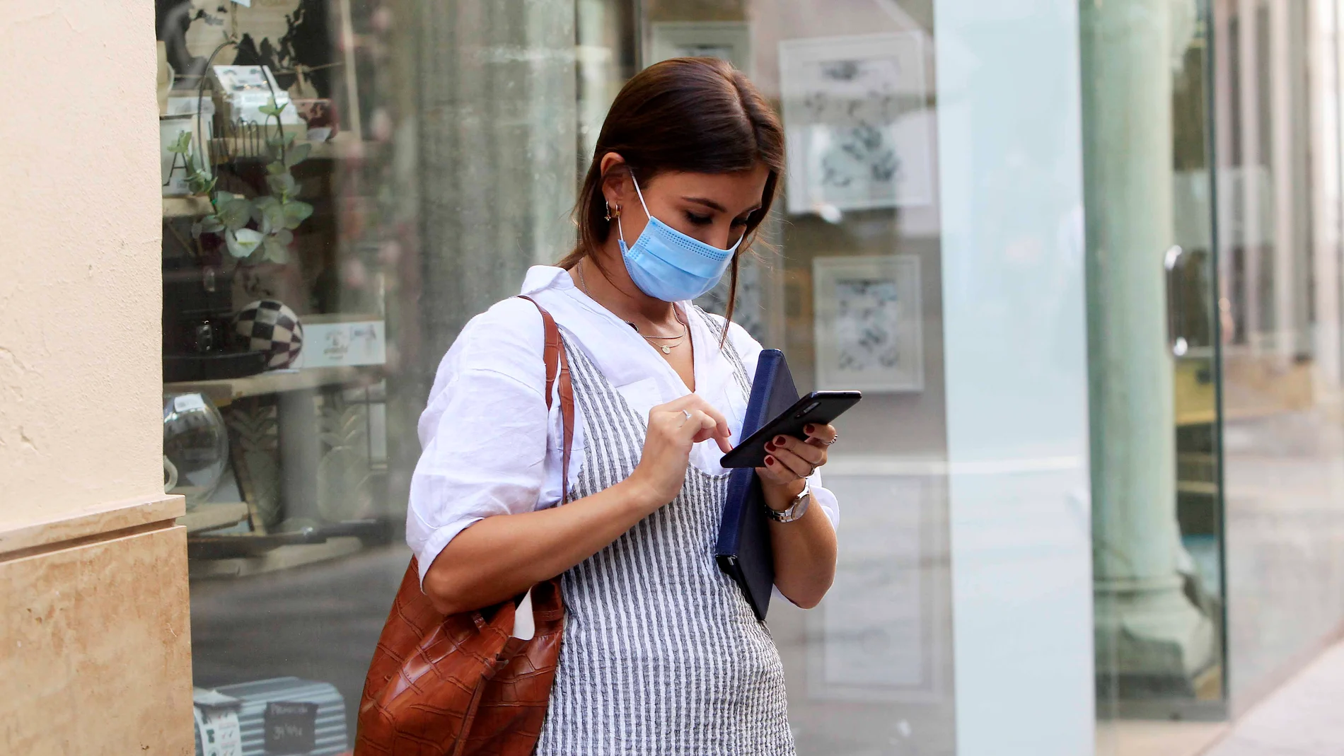 Una mujer, equipada con mascarilla, revisa su teléfono en la calle