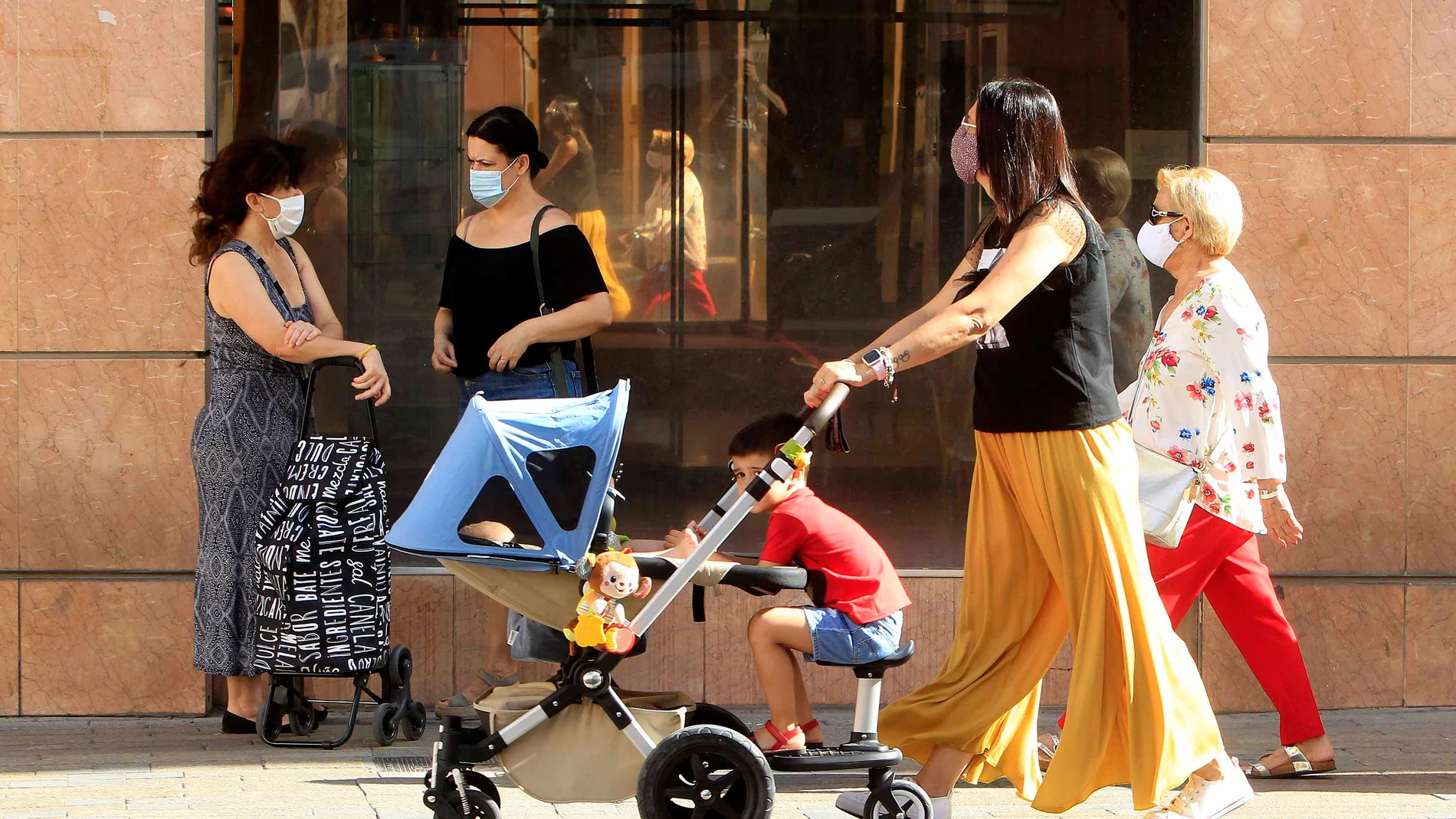 Una madre pasea por la capital hispalense, equipada con mascarilla, tras el fin del estado de alarma
