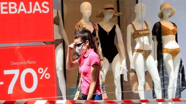 Una mujer pasea por la calle equipada con mascarilla a pleno sol