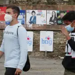 Dos jóvenes con mascarillas pasan por delante de varios carteles electorales, este viernes en Foz (Lugo)