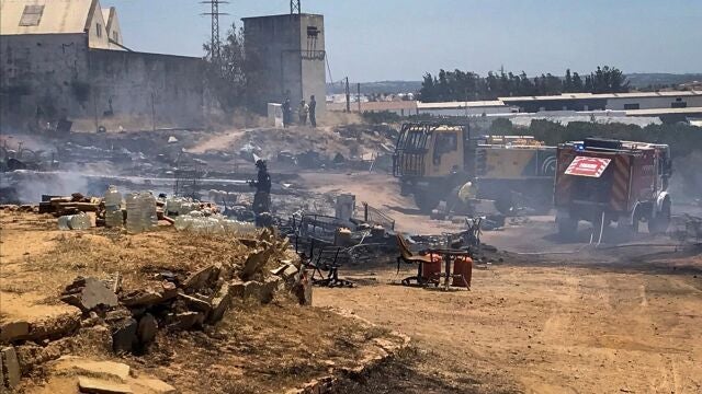 Miembros de los servicios de bomberos extinguen las llamas tras el el segundo incendio declarado en un asentamiento chabolista de Lepe esta semana