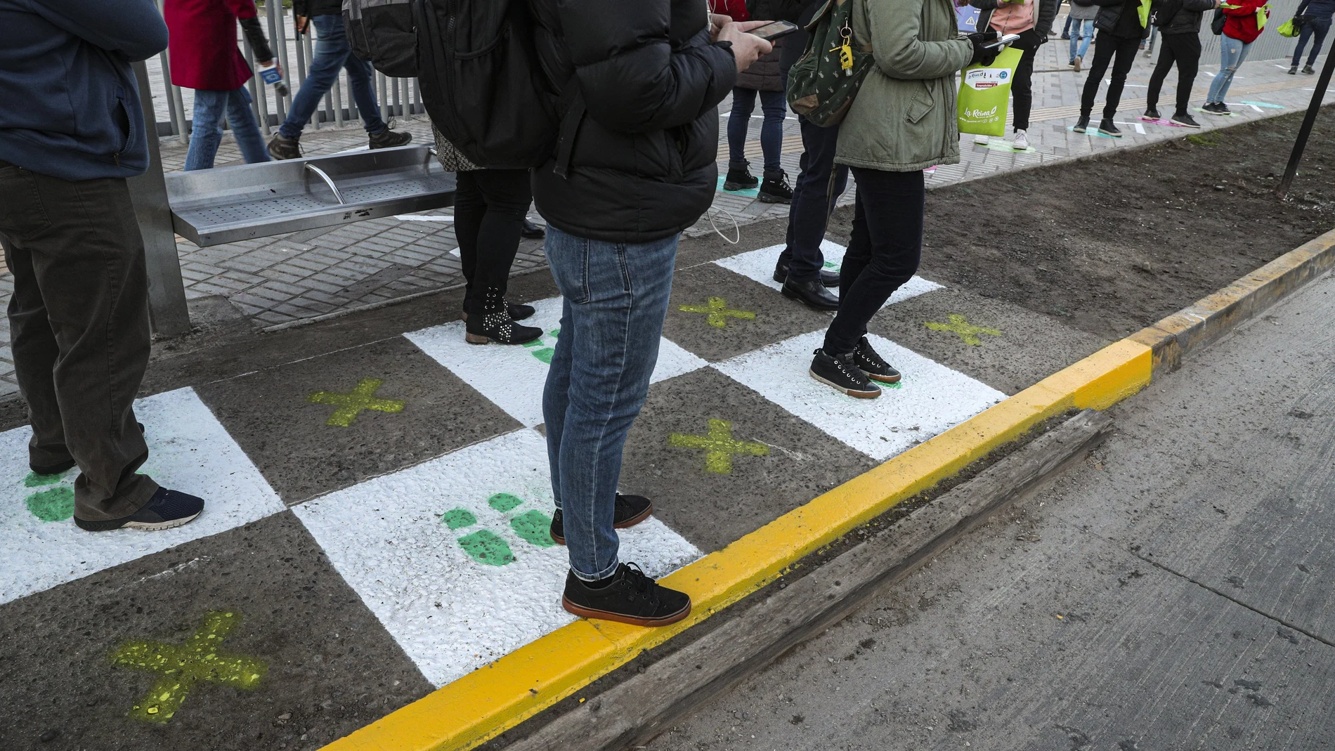 People stand on squares that help for residents to maintain a safe social distance at a bus stop La Reina borough of Santiago, Chile, Tuesday, July 28, 2020. As the Chilean government put in place a roadmap to rolling back on quarantine measures, various neighborhoods in Santiago will begin to ease on the new coronavirus lockdown on Tuesday. (AP Photo/Esteban Felix)