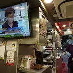 Una empleada de un restaurante entrega comida para llevar mientras en la televisión se emite el discurso de la líder de Hong Kong, Carrie Lam