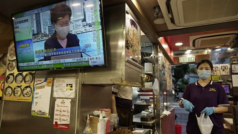 Una empleada de un restaurante entrega comida para llevar mientras en la televisión se emite el discurso de la líder de Hong Kong, Carrie Lam