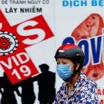 Una mujer con mascarilla pasa por un cartel que alerta sobre la covid-19 en Hanoi